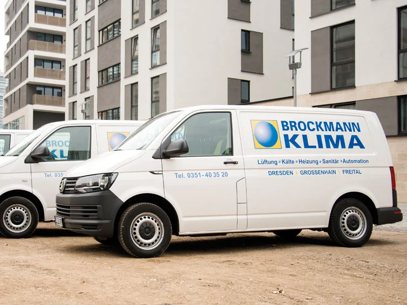 Weiße Firmentransporter mit Brockmann-Klima-Beschriftung vor einem Neubau